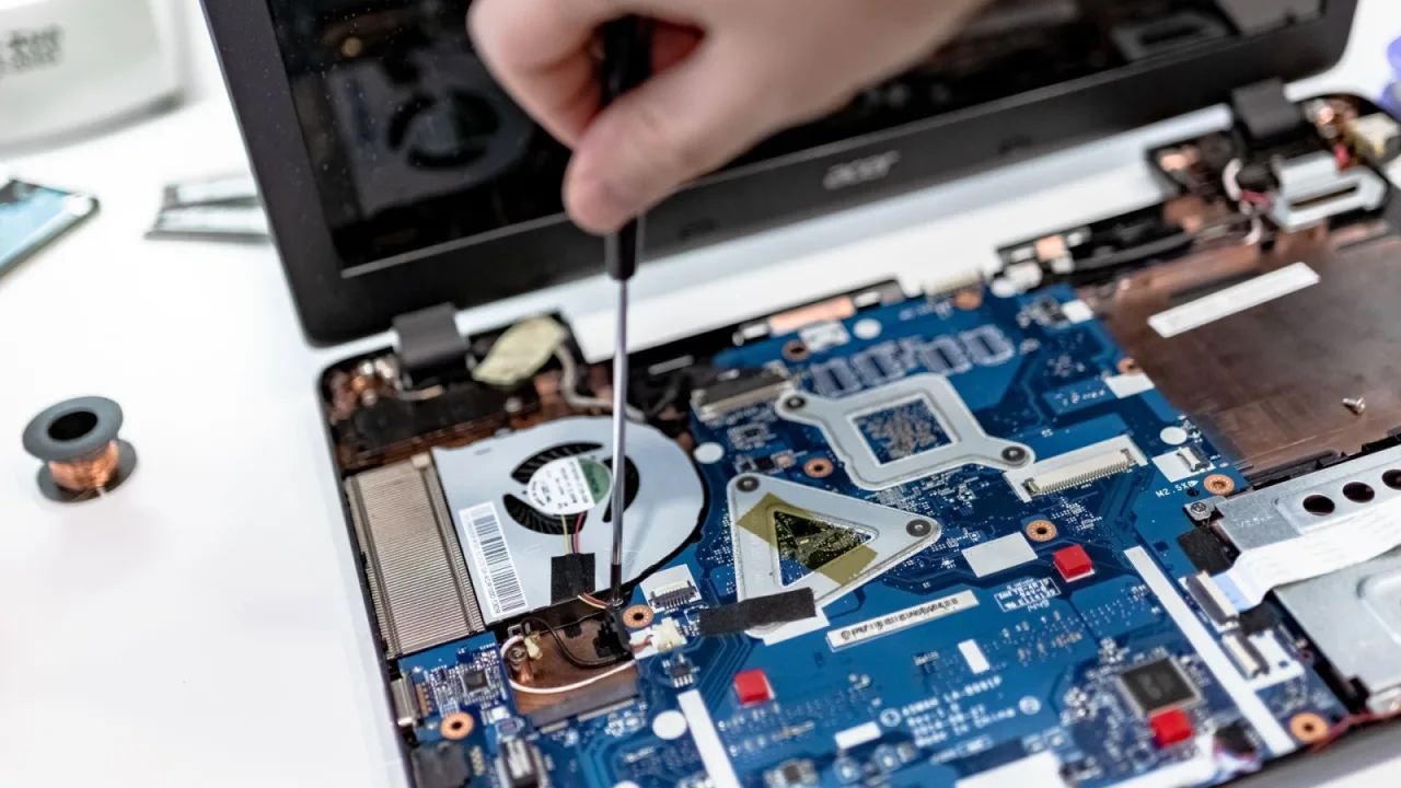 Dłoń ze śrubokrętem przy płycie głównej laptopa